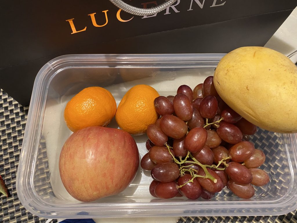 A container with various fruits including apple, grapes, mango, and oranges.