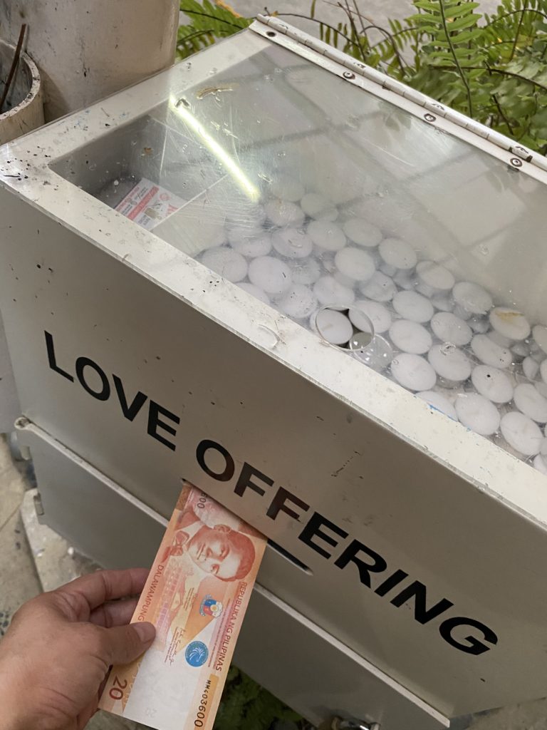 Hand placing money into a love offering box filled with candles.