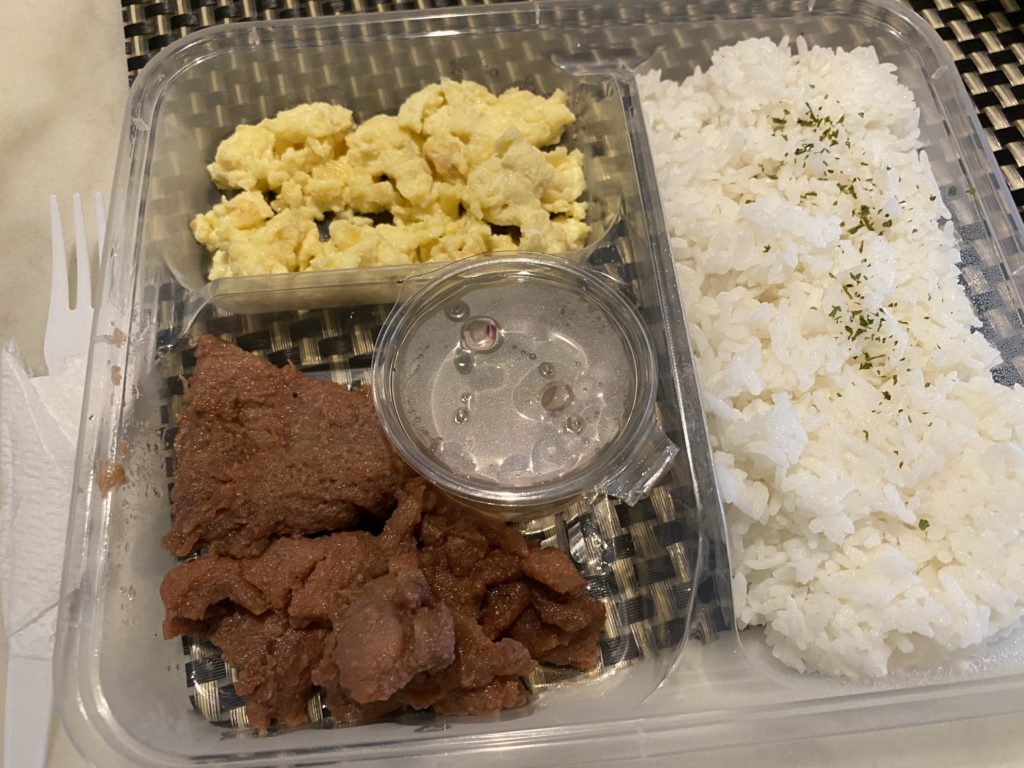 A bento box with rice, refried beans, scrambled eggs, and a creamy sauce.