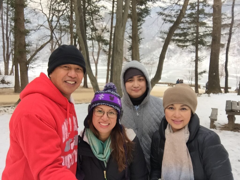 A smiling family of four dressed warmly in a forest.