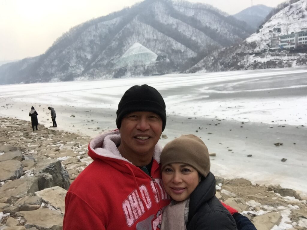 A couple posing by a snowy mountain lake in winter.