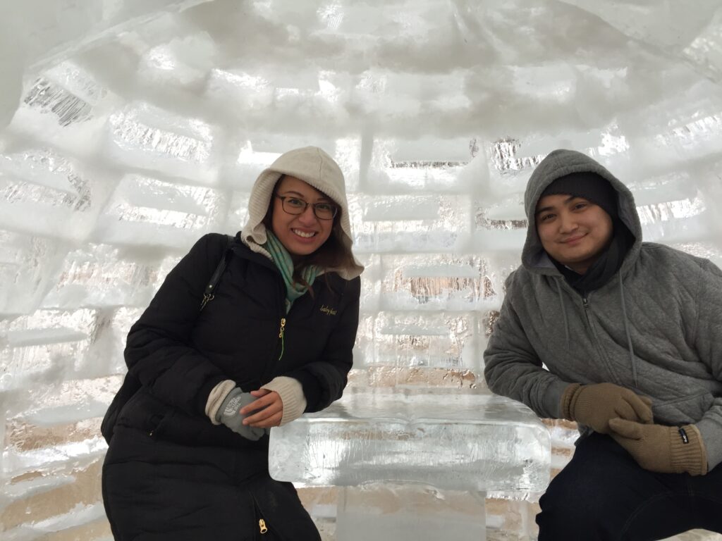 Two people sitting inside an igloo made of ice blocks.